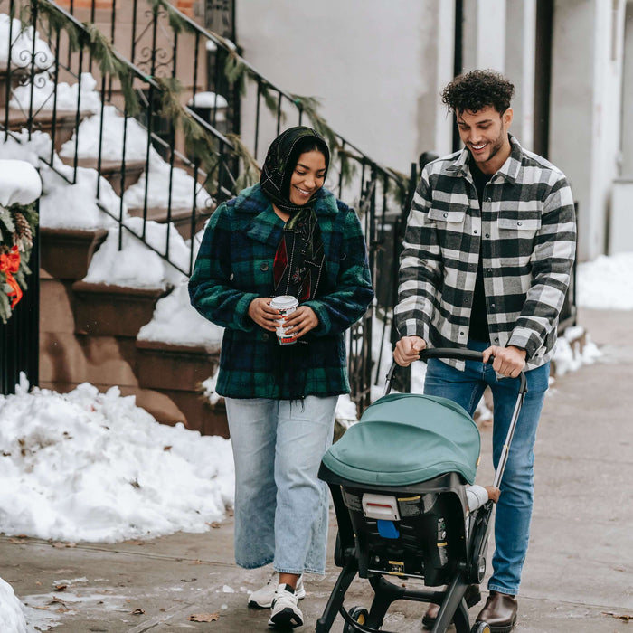 a couple walking their baby in a stroller in the snow 