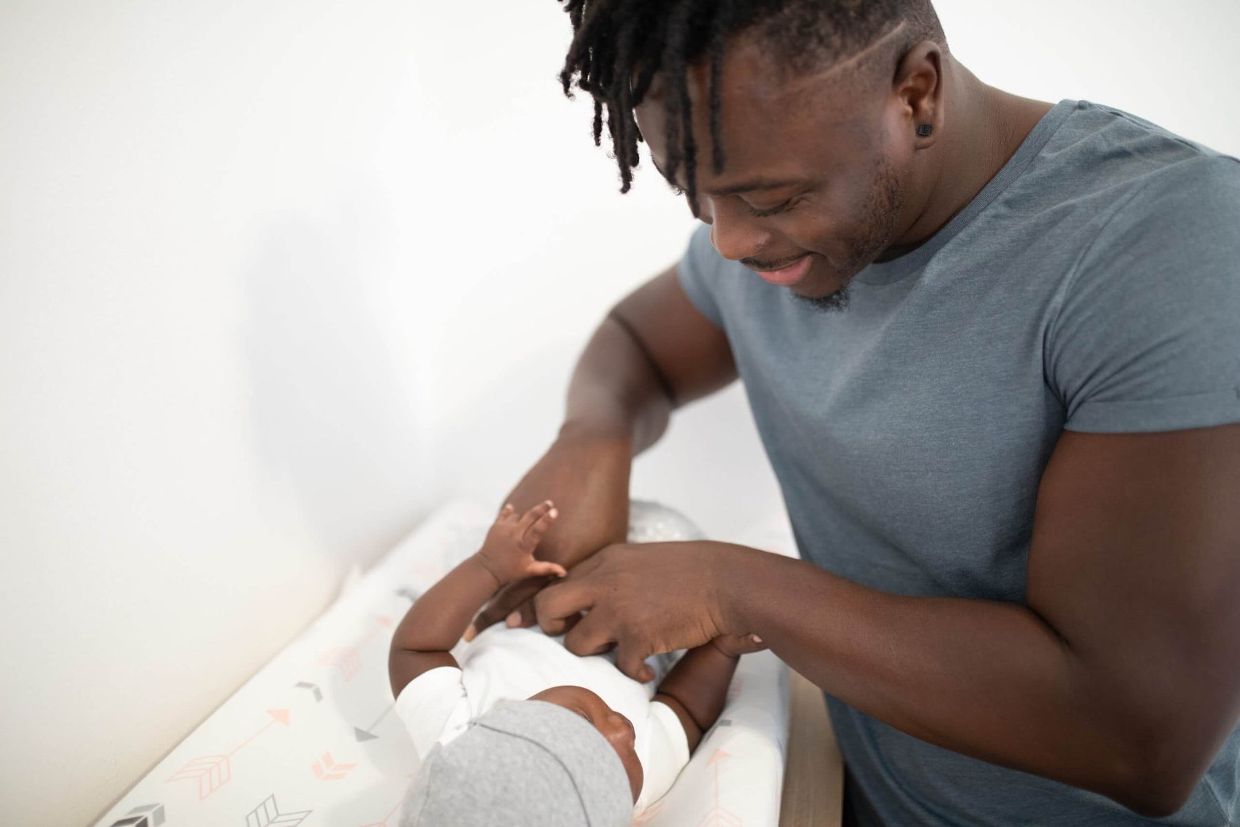 Dad changing his baby on a changing pad and smiling 