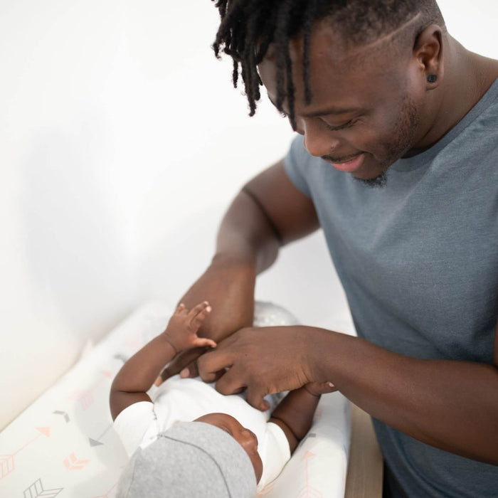 Dad changing his baby on a changing pad and smiling 