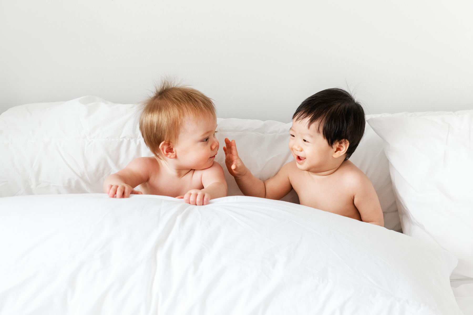 two babies laughing in a bed with white sheets