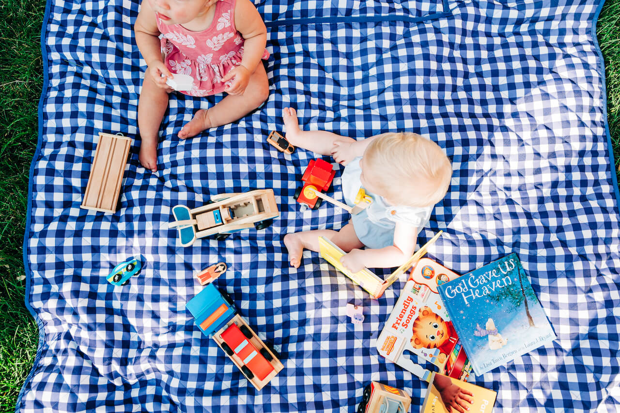 two 9 month olds playing on a blanket with toys 