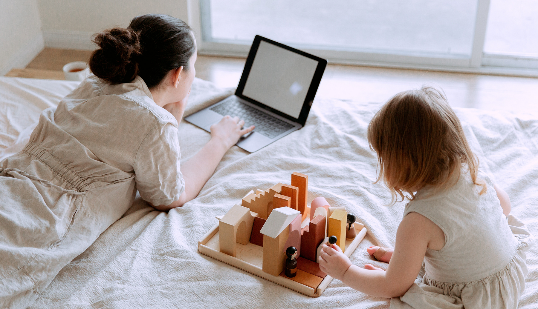 Mom looking on the computer with toddler playing with sustainable toys