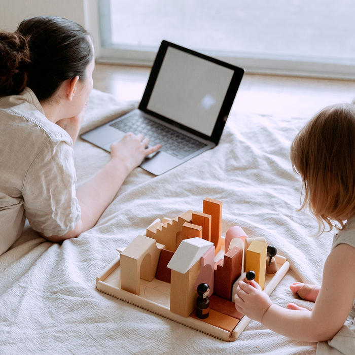 Mom looking on the computer with toddler playing with sustainable toys