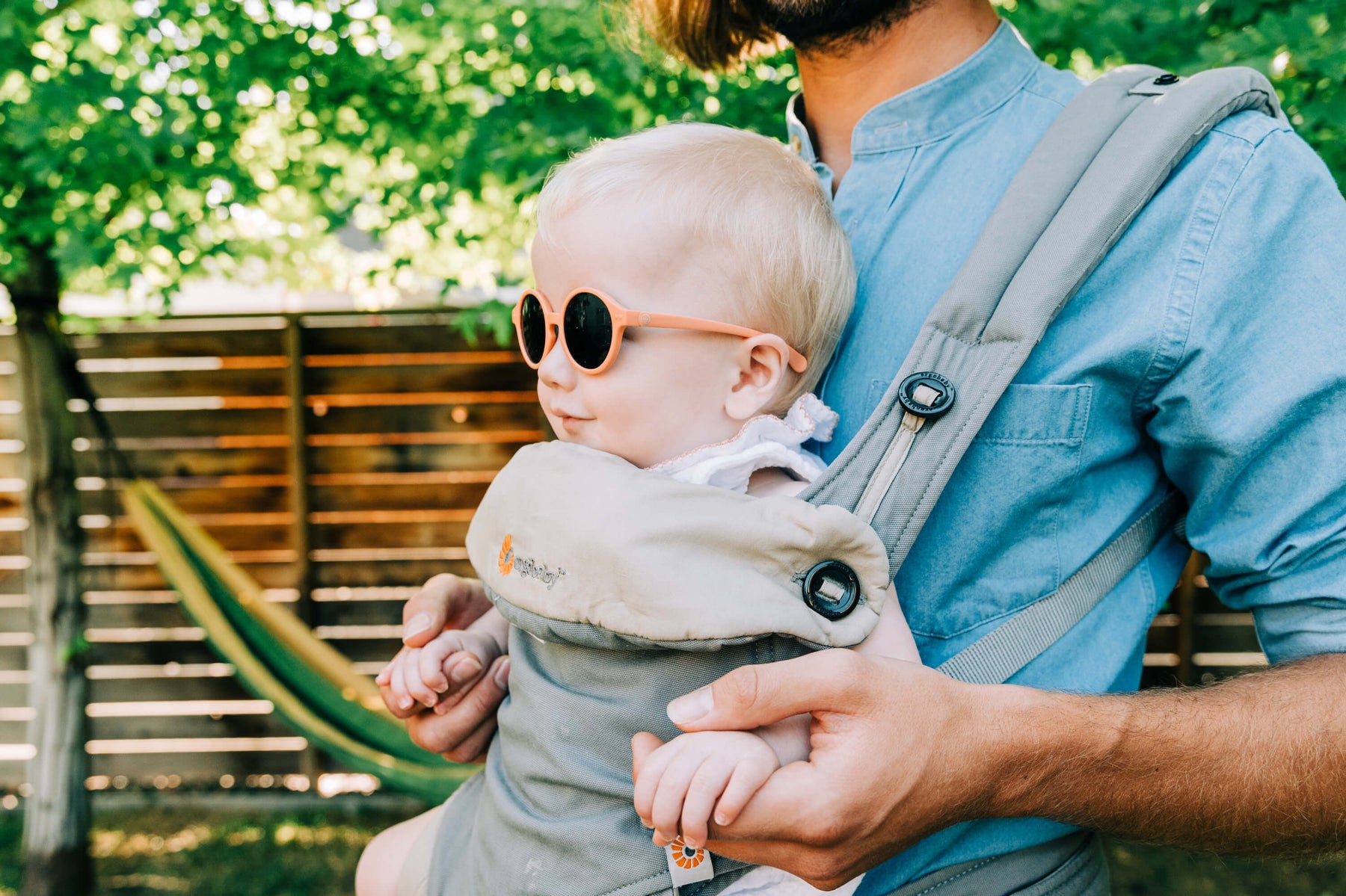 blond baby wearing glasses during the spring in a baby carrier