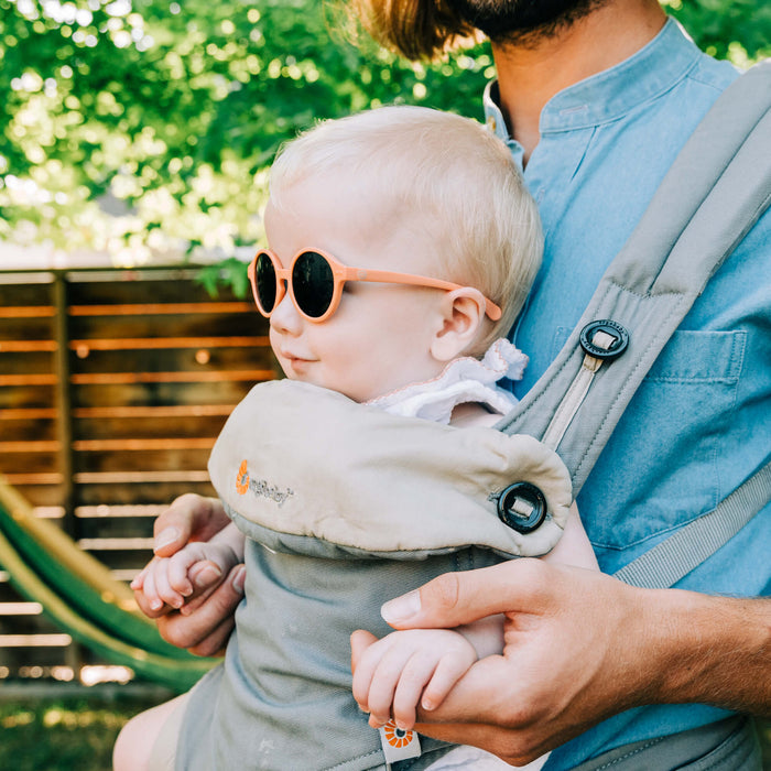 blond baby wearing glasses during the spring in a baby carrier